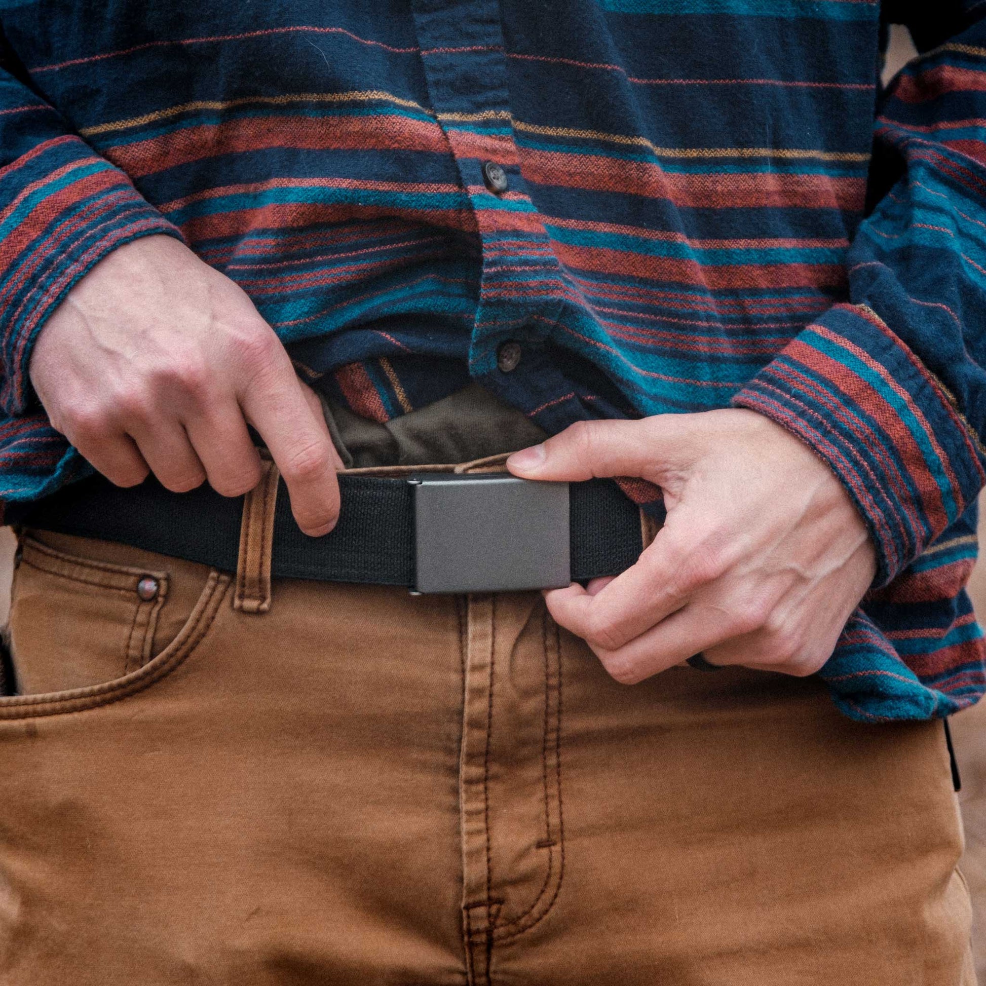 Person adjusting a belt with a plaid shirt and brown pants