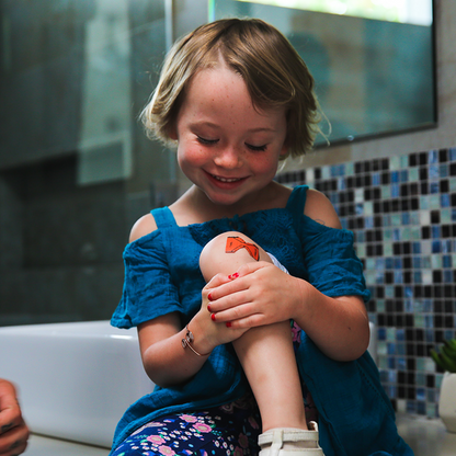 Child in a blue dress holding a toy in a bathroom with tiled walls.