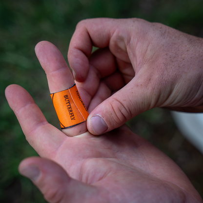 Hand holding a small orange bandage with 'Butterfly' branding against a blurred natural background.