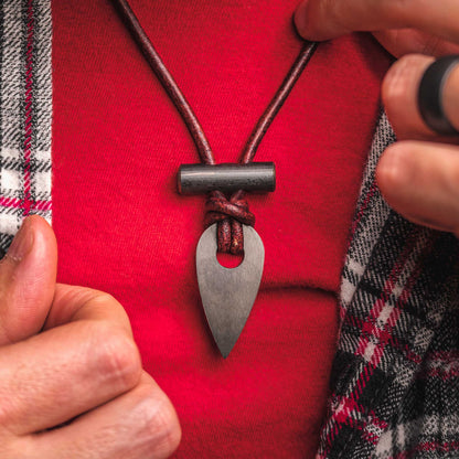 Necklace with a metal pendant held by a person against a red background