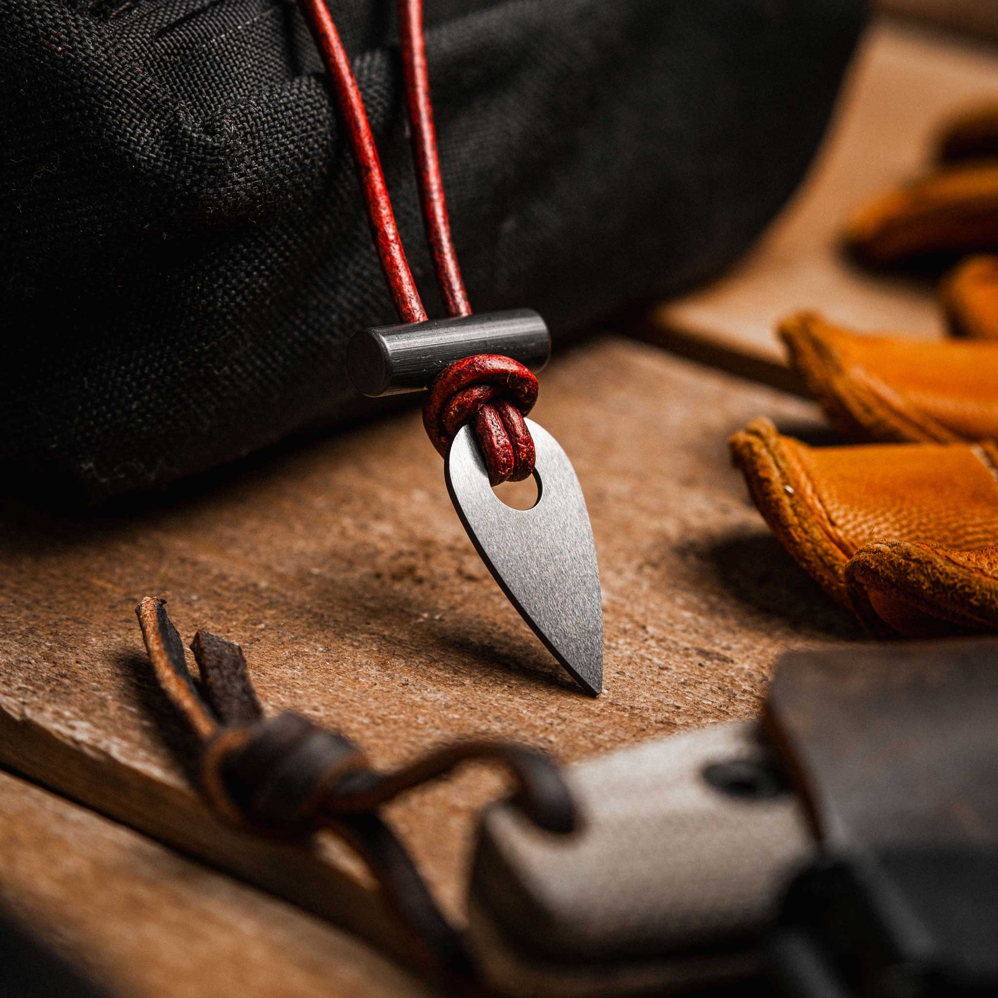 Metallic arrowhead pendant on a red cord with leather and fabric background