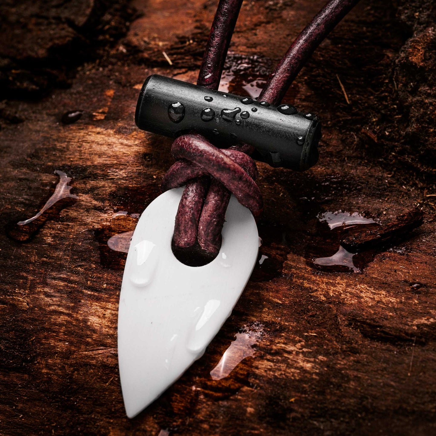 Necklace with a white arrowhead pendant and black and red cord on a wooden surface