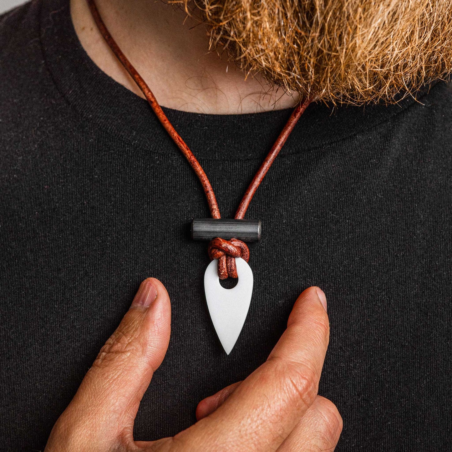 Person wearing a necklace with a white pendant on a black background