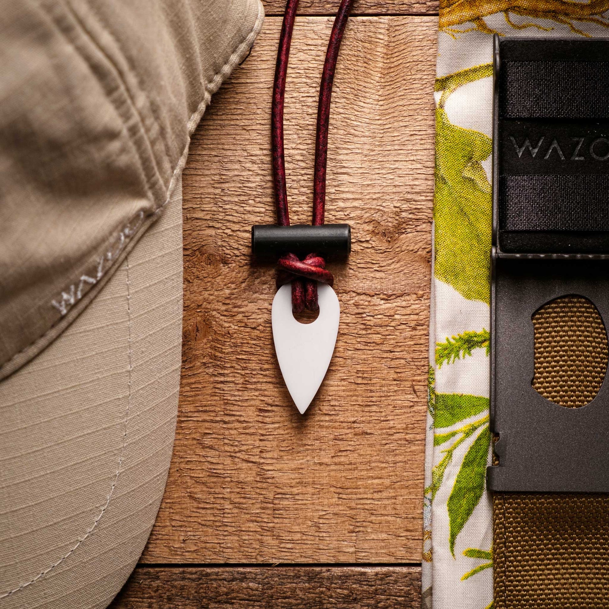 Arrowhead pendant on a red cord with a cap, fabric, and pouch in the background.