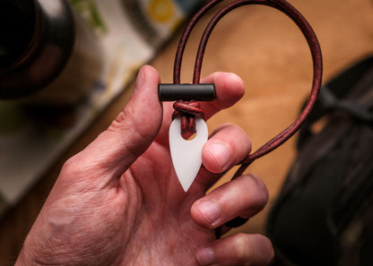 Hand holding a necklace with a white pendant and brown cord